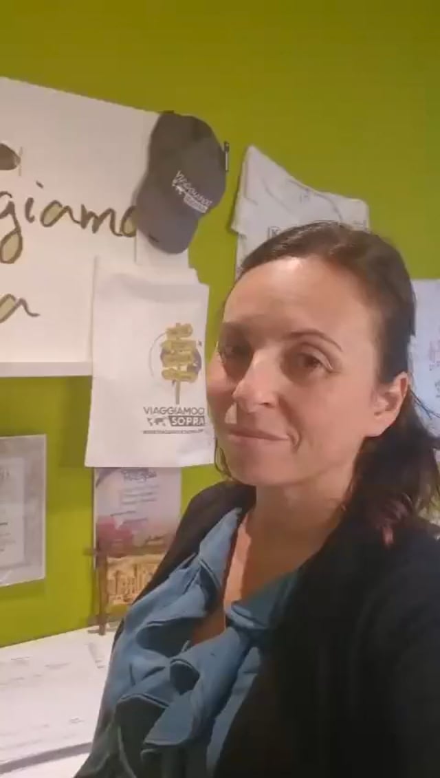 Fermo immagine del video: una donna parla alla fotocamera in agenzia, davanti alla parete verde con il logo Viaggiamo Ci Sopra.